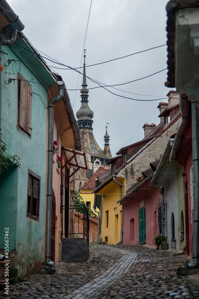 Wąska kamienna uliczka z kolorowymi budynkami i kościołem - obrazy, fototapety, plakaty 