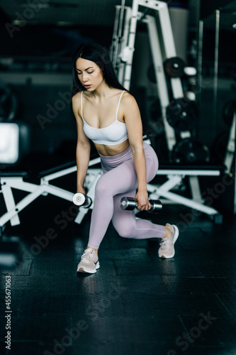 A young woman doing sit-ups with a weight dumbells in the sports gym. Technique of squats with weight