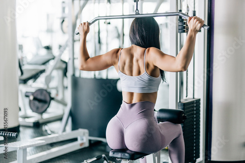 Fitness young woman working out in gym doing exercise for back. Athletic girl doing lat pulldown