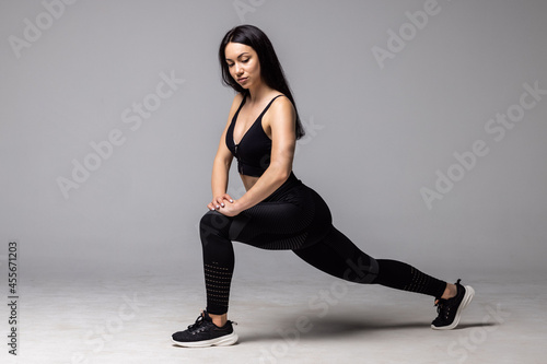 Fototapeta Naklejka Na Ścianę i Meble -  Athletic woman doing lower body sport exercise, stretching legs, warming up muscles for flexibility isolated on gray background