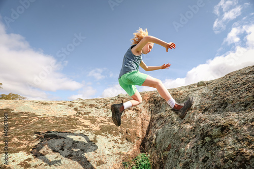 Boy running and jumping on rocks under cloudy blue sky in nature