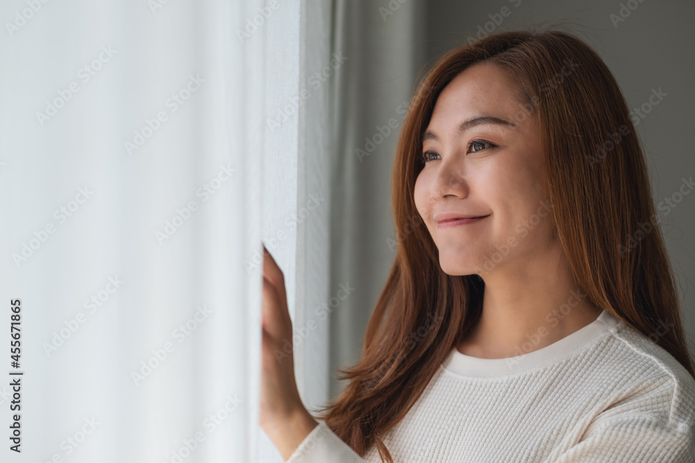 A beautiful young asian woman touching curtain and looking outside the window A beautiful young asian woman touching curtain and looking outside the window