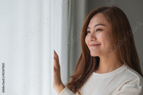 A beautiful young asian woman touching curtain and looking outside the window