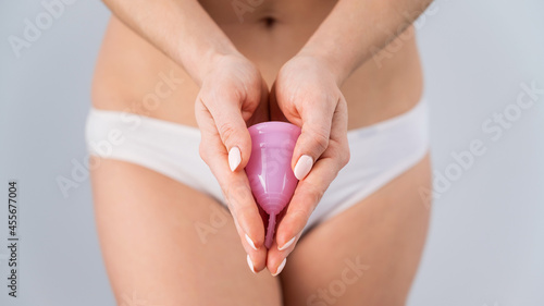 Close-up of a woman in white cotton panties holding a pink menstrual cup against a white background. Alternative to tampons and pads