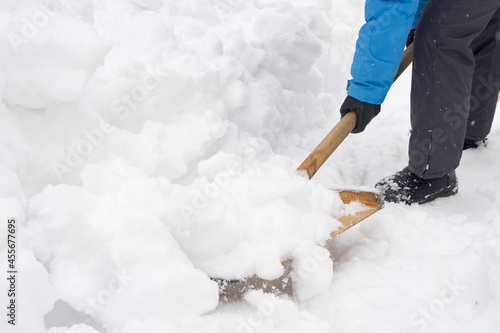 A woman cleans a path from snowdrifts with a wooden shovel on a winter day.