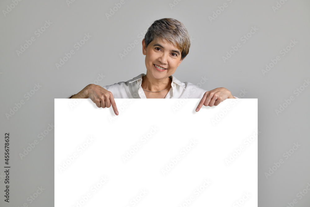 Attractive middle aged Asian woman pointing fingers at blank signboard isolated on white background. looking at the camera Attractive middle aged Asian woman pointing fingers at blank signboard isolated on white background. looking at the camera