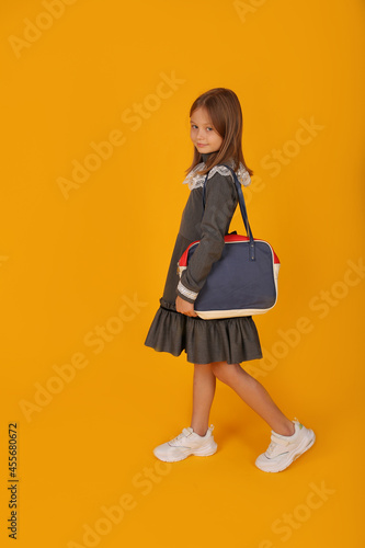 a beautiful brown-haired girl in a gray school dress and a briefcase in her hands