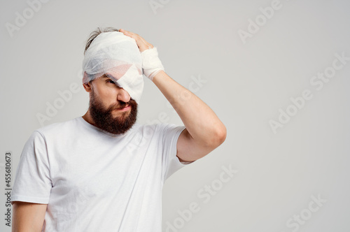 bearded man with bandaged head and eye hospitalization light background