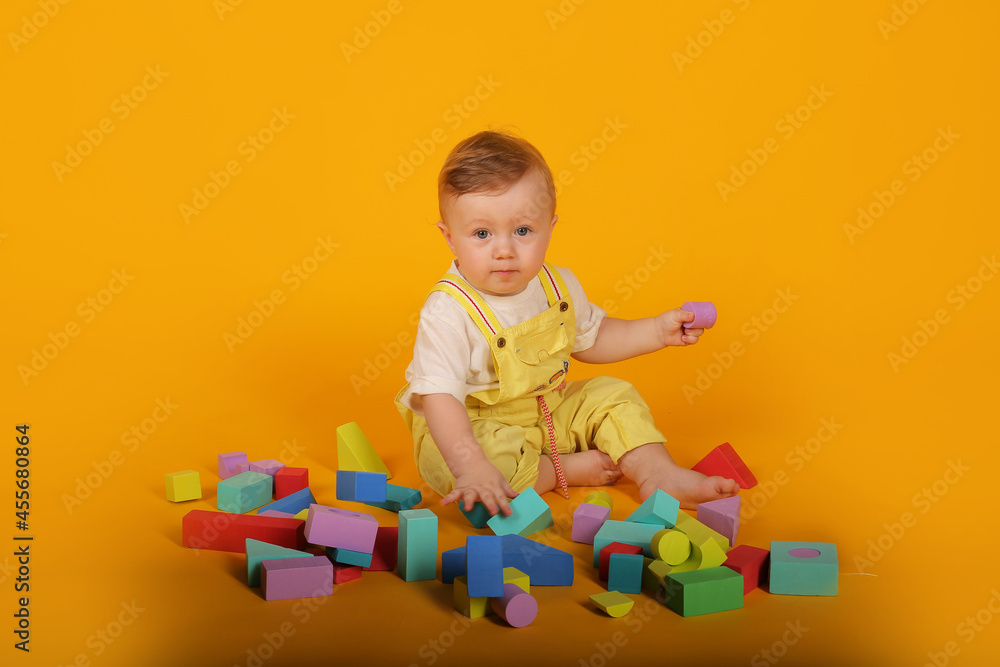 a beautiful blue-eyed little boy in a yellow suit plays with colorful toys a beautiful blue-eyed little boy in a yellow suit plays with colorful toys
