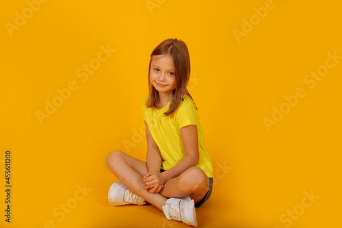 a beautiful brown-haired girl in a yellow T-shirt and shorts is sitting on a yellow background