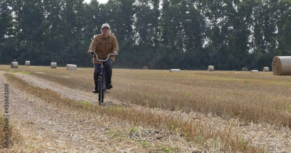 Cycling, countryside. An elderly woman rides a bicycle through a mown wheat field covered with rolls of straw. Siberia. Cycling, countryside. An elderly woman rides a bicycle through a mown wheat field covered with rolls of straw. Siberia.