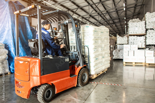 A man on a forklift works in a large warehouse, unloads bags of raw materials © xartproduction