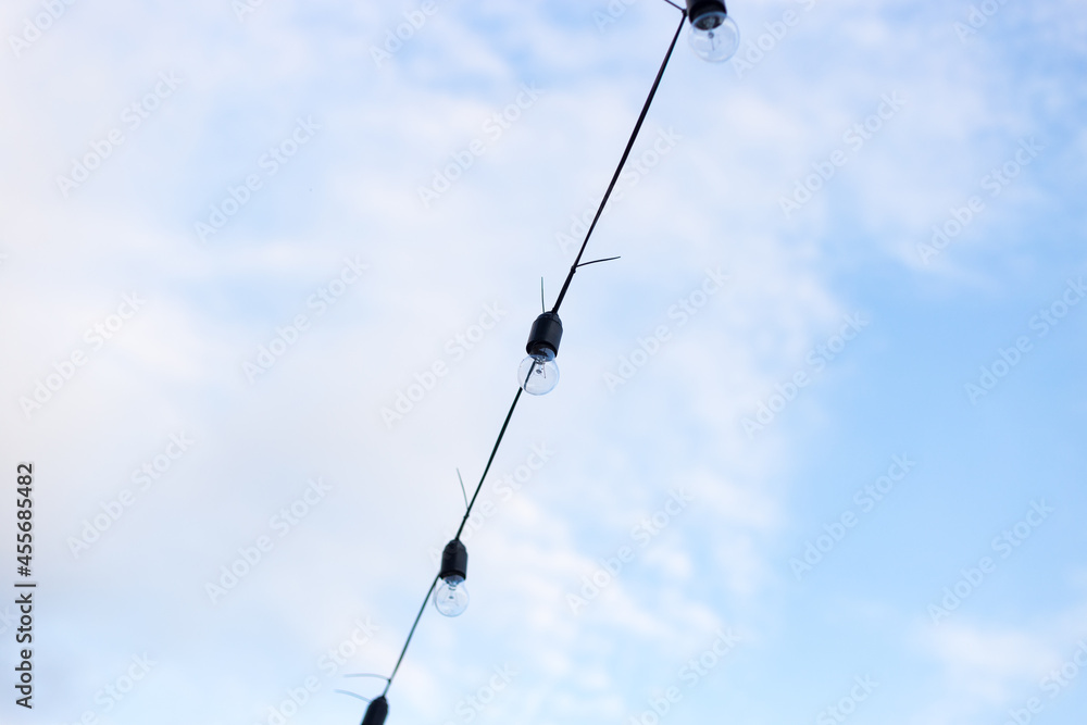 Lamps in series with the blue sky background . Street electric garland against the sky. One row of street lights for lighting Lamps in series with the blue sky background . Street electric garland against the sky. One row of street lights for lighting