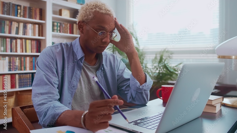 Frustrated sad young afro american businessman looking at laptop screen and holding his head with his hand feeling stressed and depressed. Man in office reads bad news, bank debt reports or bankruptcy Frustrated sad young afro american businessman looking at laptop screen and holding his head with his hand feeling stressed and depressed. Man in office reads bad news, bank debt reports or bankruptcy