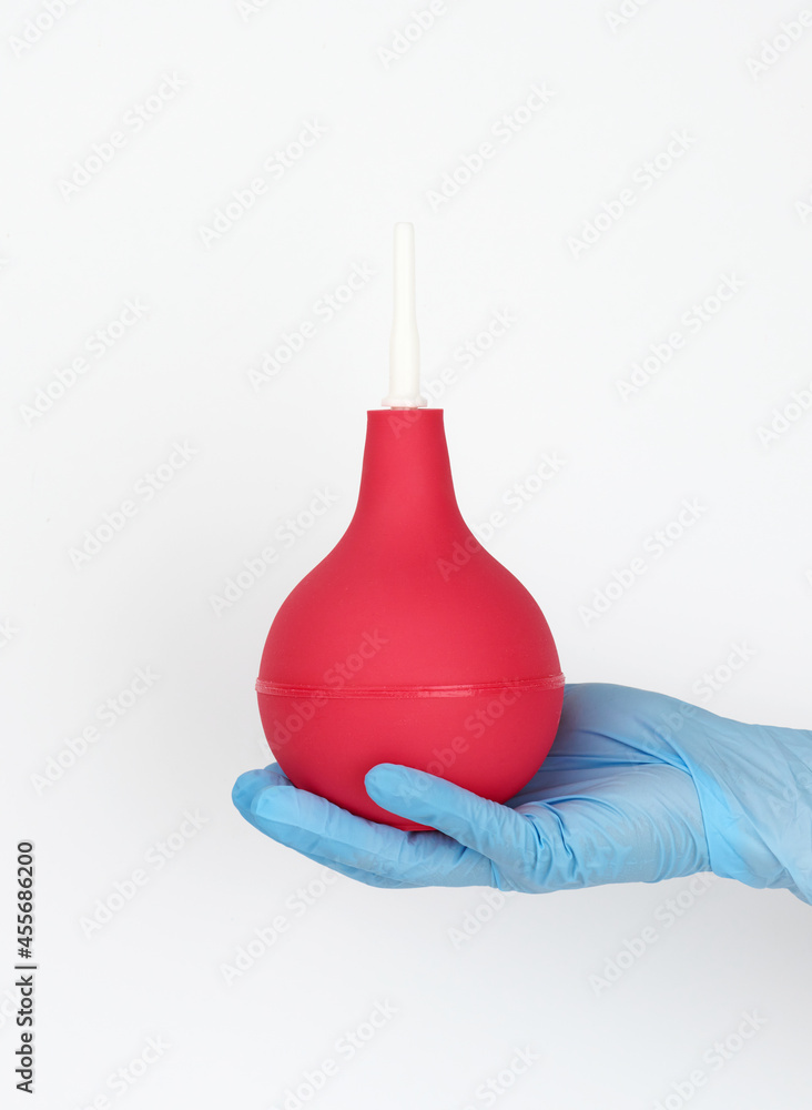 hand in a blue medical glove holds a pink rubber enema on a white background hand in a blue medical glove holds a pink rubber enema on a white background