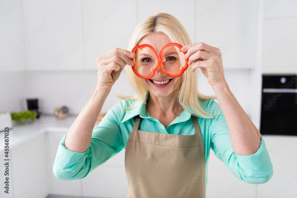 Photo of mature attractive woman happy positive smile fooling grimace look eye binoculars pepper slices cooking indoors