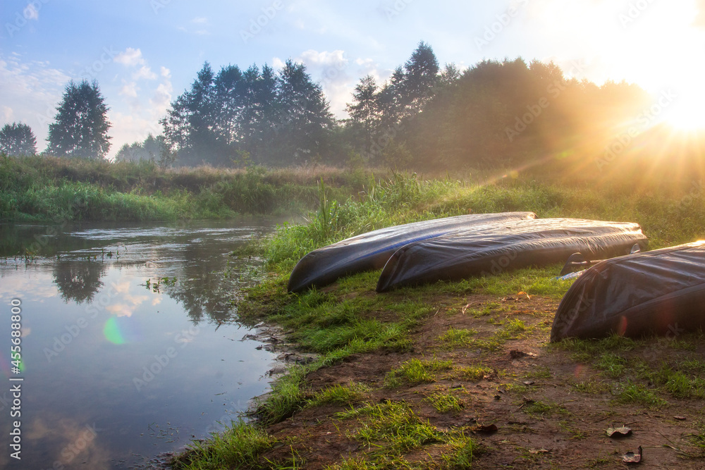 Travelling by kayaks. Misty sunrise on the beach of the river with kayaks. Summery travel on the water.