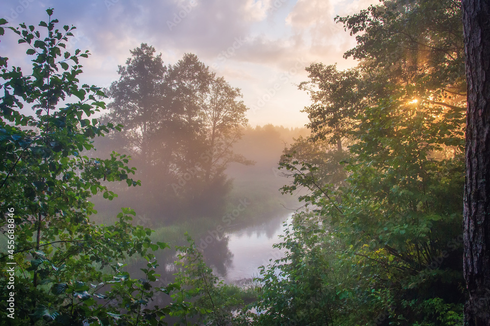 Autumn misty sunrise. Landscape of misty river in the woodland. Nature in first days of autumn. Low sky with small dark clouds.