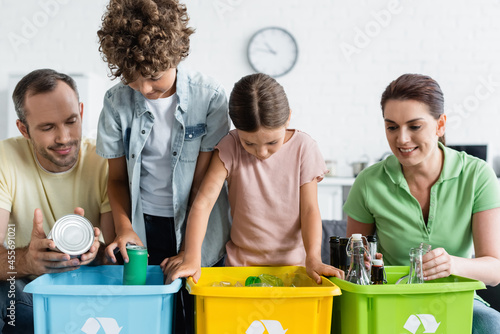 Family with kids sorting trash in boxes with recycle sign at home