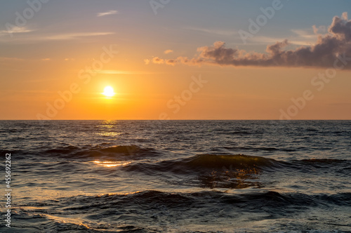 Sunset over the sea. Reflection of sunlight in the sea waves. Red and yellow sky in the rays of the sunset.