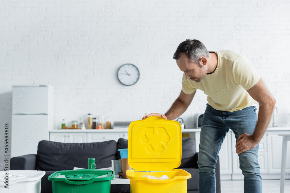 Man looking at trash can with recycle sign in kitchen Man looking at trash can with recycle sign in kitchen