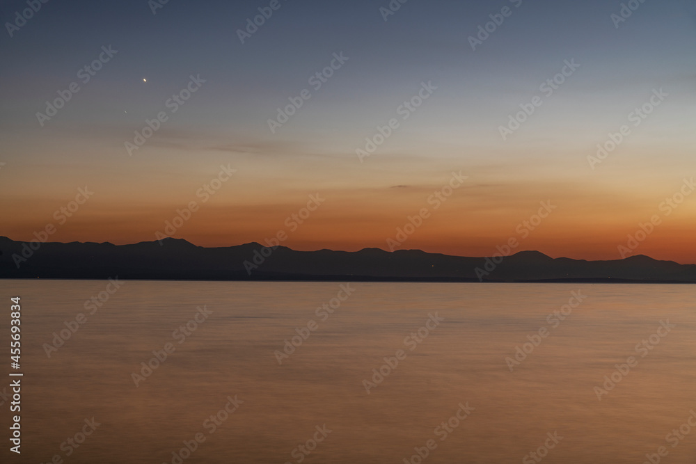 Beautiful sunset on the lake with silhouette mountais, long exposure water.
