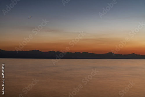Beautiful sunset on the lake with silhouette mountais, long exposure water. © Inga Av