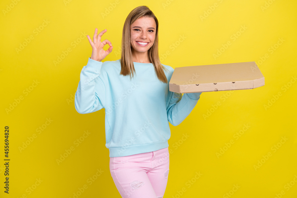 Portrait of attractive cheerful girl holding order tasty pizza showing ok-sign ad isolated over bright yellow color background Portrait of attractive cheerful girl holding order tasty pizza showing ok-sign ad isolated over bright yellow color background