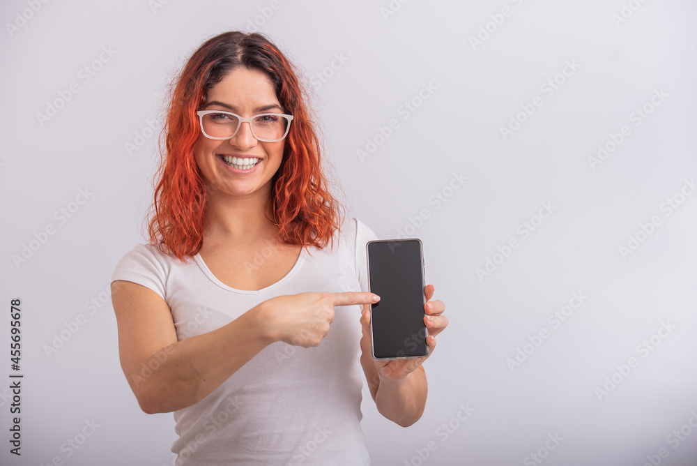A Caucasian woman points to a smartphone with a blank screen on a white background A Caucasian woman points to a smartphone with a blank screen on a white background