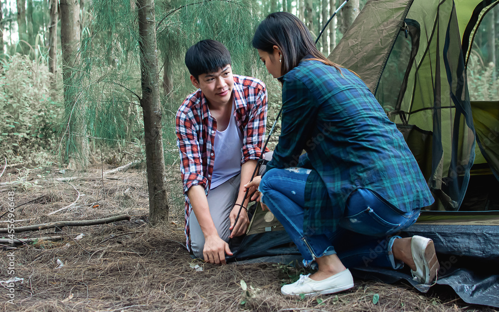 Asian handsome male and beautiful female pitching tent together while camping in forest on holiday vacation. Lifestyle, Couple and Summer Concept. Asian handsome male and beautiful female pitching tent together while camping in forest on holiday vacation. Lifestyle, Couple and Summer Concept.