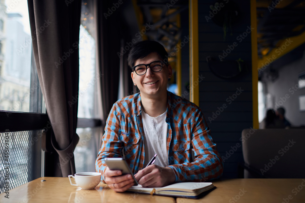Millennial mobile phone user sitting at the table with notebook while preparing for exams. Smartphone application, modern technology for learning Millennial mobile phone user sitting at the table with notebook while preparing for exams. Smartphone application, modern technology for learning