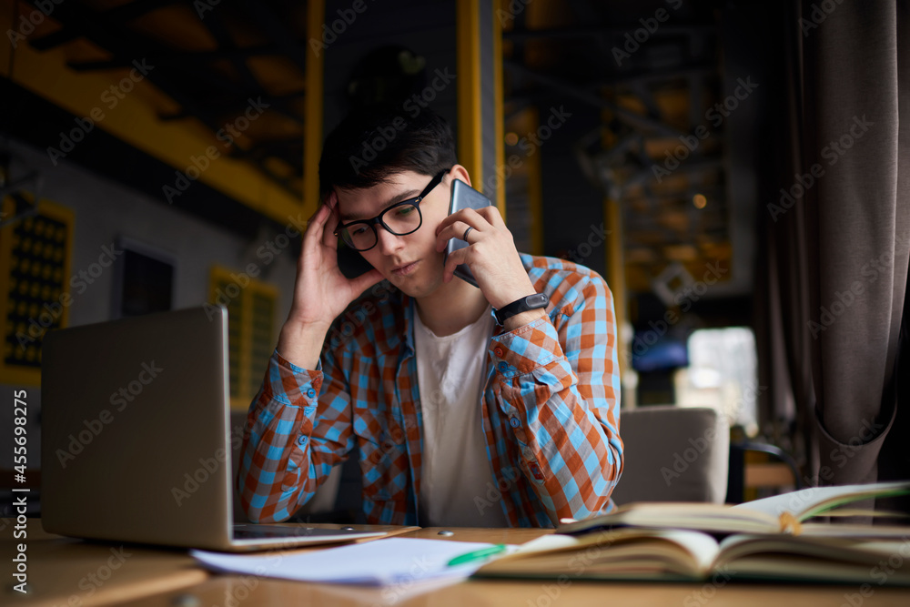 Young freelance worker calling via mobile phone while holding documents in hand. Small owner working remote in coffee shop interior Young freelance worker calling via mobile phone while holding documents in hand. Small owner working remote in coffee shop interior