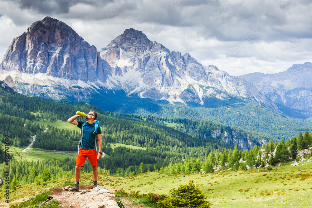 Hiking Man relaxing and drinking water after trekking with Dolomites mountains in the background, Italy.