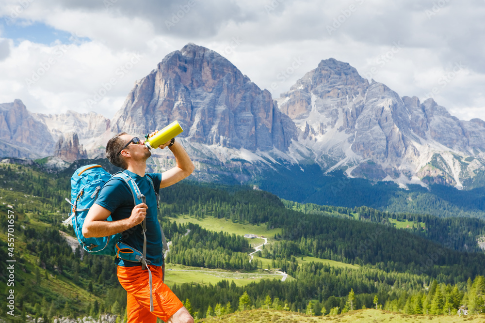 Man relaxing and drinking water after trekking with Dolomites mountains in the background, Italy.