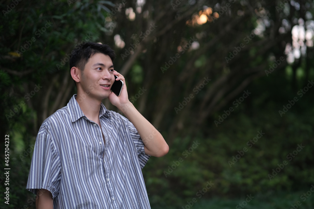 Asian young man on the phone in natural park, smiling happily