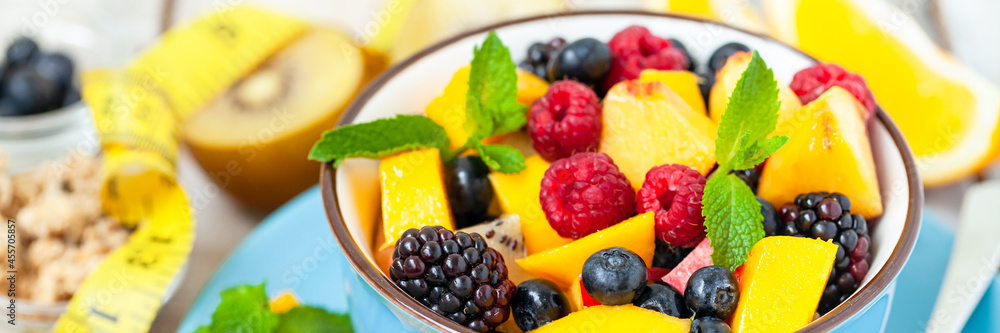 Concept of low calories delicious desserts. Summer fresh bowl with colorful fruit salad. Healthy natural organic food. Tasty sweet snack, light simple tasty lunch. Close up wooden background banner Concept of low calories delicious desserts. Summer fresh bowl with colorful fruit salad. Healthy natural organic food. Tasty sweet snack, light simple tasty lunch. Close up wooden background banner