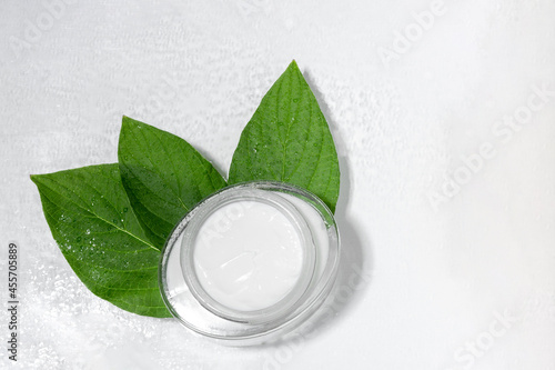 Moisturizing face and eyelid cream with natural extracts. Glass cosmetic jar with leaves. Natural cosmetic product