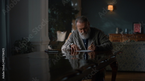 Pensive old man working documents in cabinet. Senior man writing letter at home