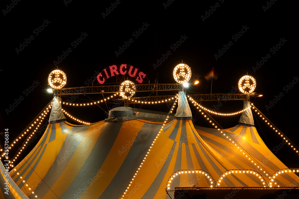 A circus tent at night with its colorful lights on