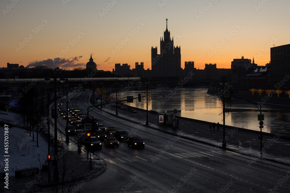 Obraz premium Morning winter urban landscape. Silhouette of Stalin's high-rise on Kotelnicheskaya embankment at sunrise. Morning traffic in Moskvoretskaya Embankment. Moscow, Russia.