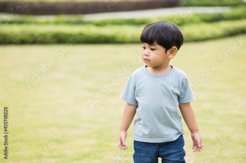 Child walking on the grass. Asian Little boy wear a blue shirt walking around. Children playing in the playground with sunlight. © Chanakon