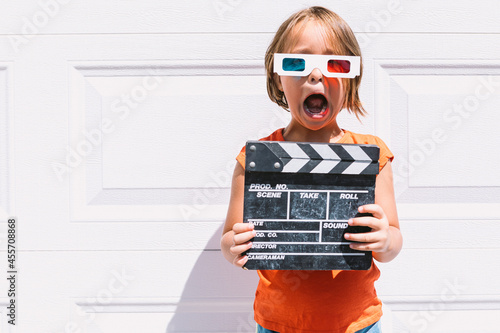 Trendy kid in 3D glasses holding clapperboard standing on wall photo