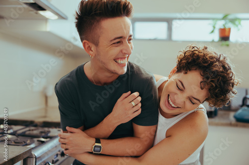 Young queer couple laughing cheerfully in their kitchen