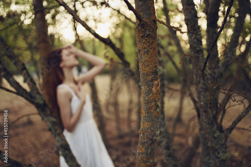 pretty woman in white dress leaning on a tree in the summer forest