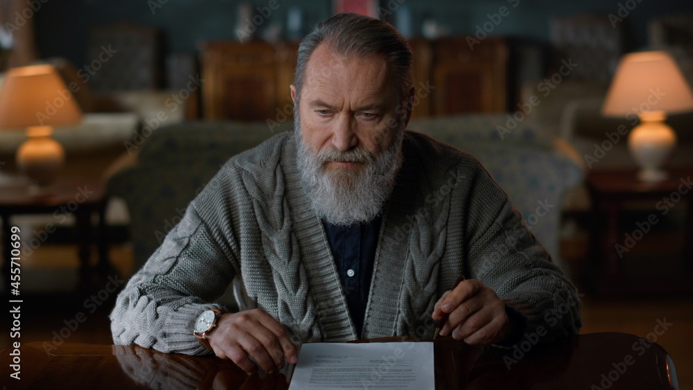 Fototapeta premium Pensive elderly gentleman doing paperwork home. Senior man signing document.
