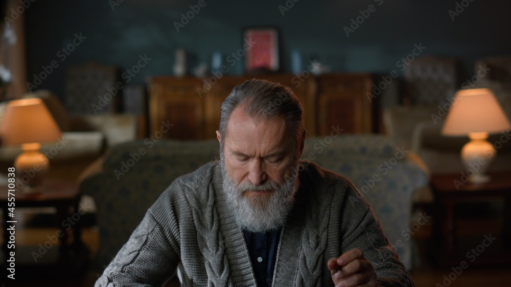 Grey haired man reading letter luxury room. Senior gentleman sitting table home.