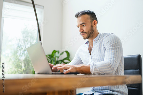 Portrait young mexican attractive businessman working at modern home office with computer laptop
