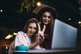 Smiling ladies sitting in restaurant with beverages and laptop