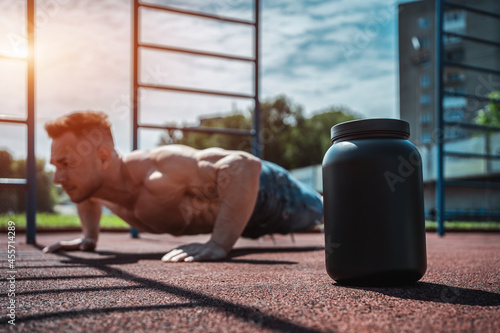 protein whey drink in black container and muscular athlete exercising outdoor photo