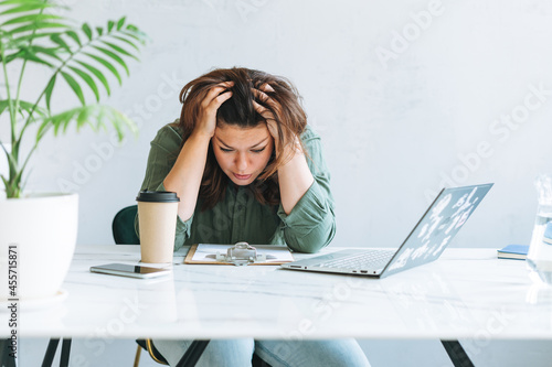 Foto Young thinking unhappy brunette woman plus size working at laptop on table with